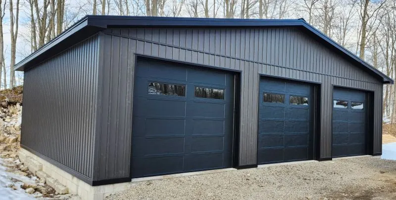 Three black insulated overhead doors on a dark pole barn