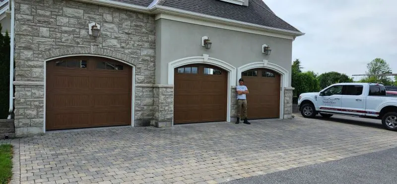 Three wood-look Clopay garage doors on a stone home