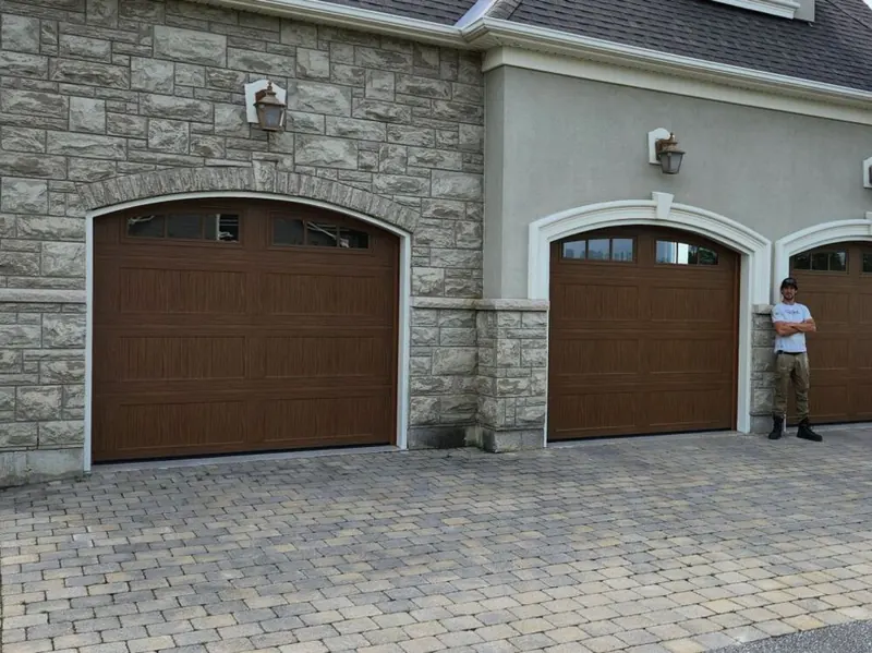 Three wood-look Clopay garage doors installed on a stone home